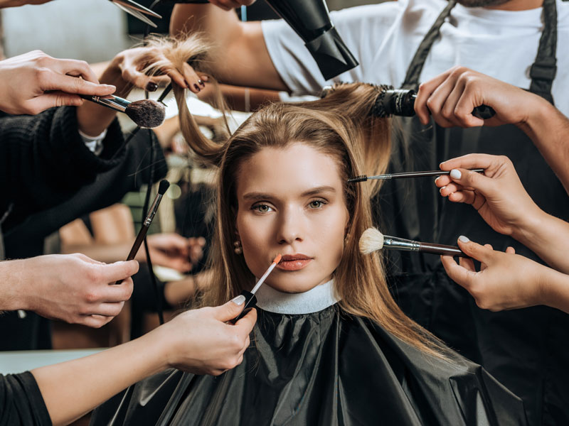 what-is-cosmetology Model surrounded by cosmetologists with makeup and hair brushes